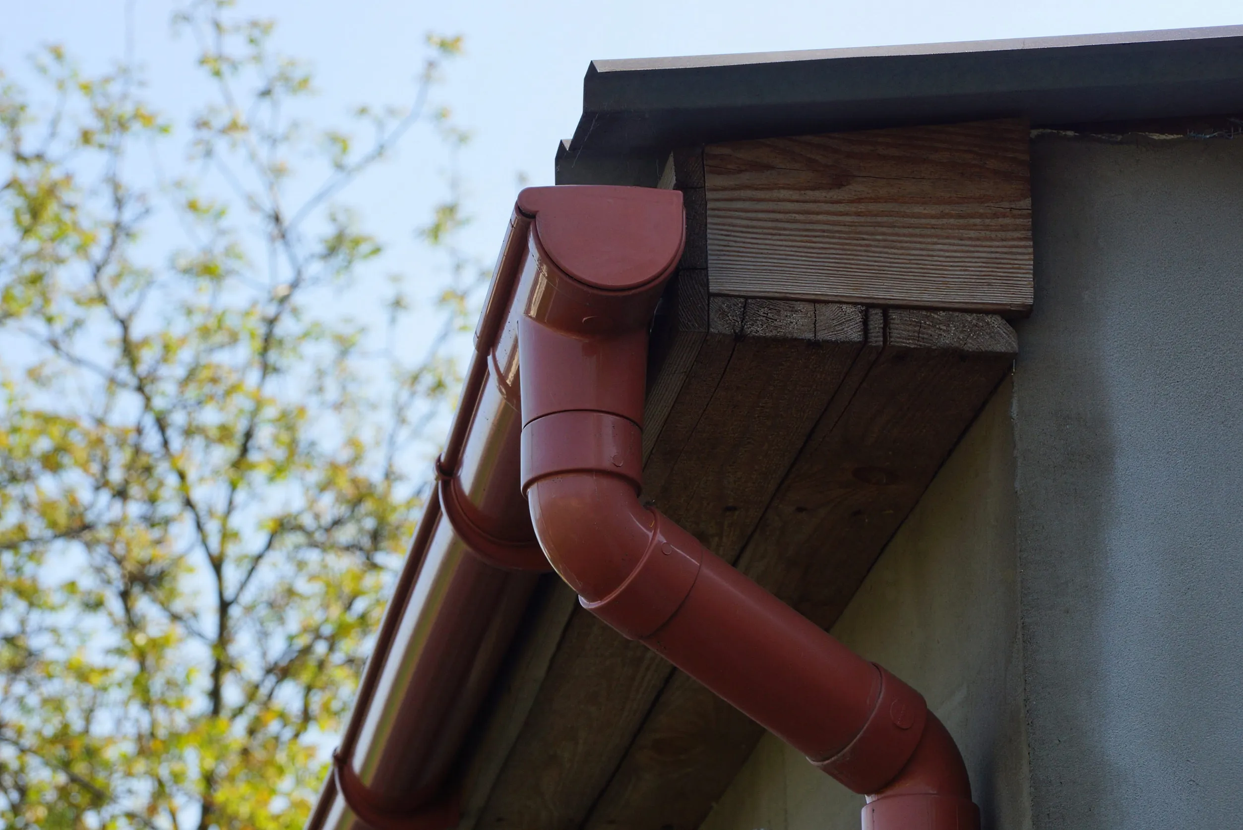 red plastic drain pipe on brown wooden roof boards near the gray wall of the house